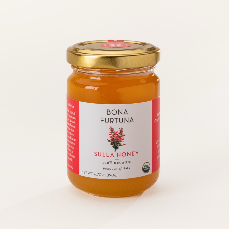 A small glass jar of honey with a gold lid on a plain background